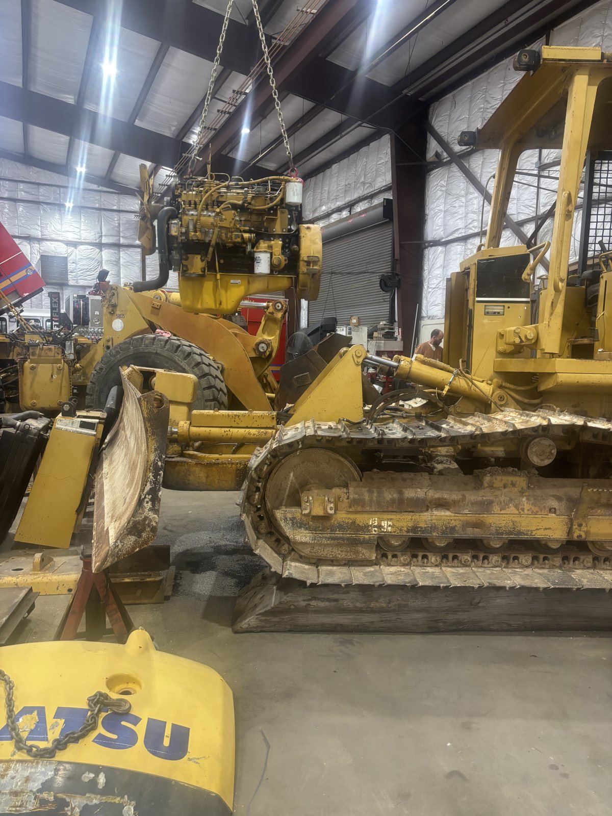 A Komatsu excavator parked in a shop bay, tracks and cab visible